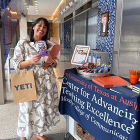 A woman stands in front of a CATE booth as she smiles and holds momentoes from the event. 